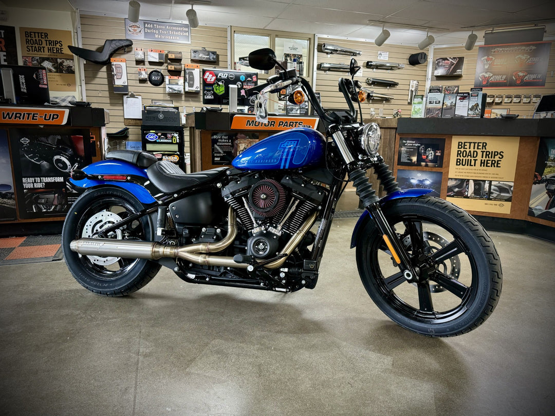 A black motorcycle with the focus on the exhaust system, which is silver in color. The motorcycle is parked against a plain wall backdrop.