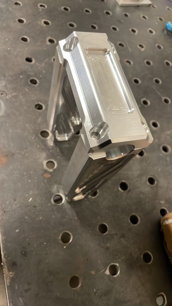 A pair of silver motorcycle bar risers placed on a wooden surface, with engraved details and ratios on the side.