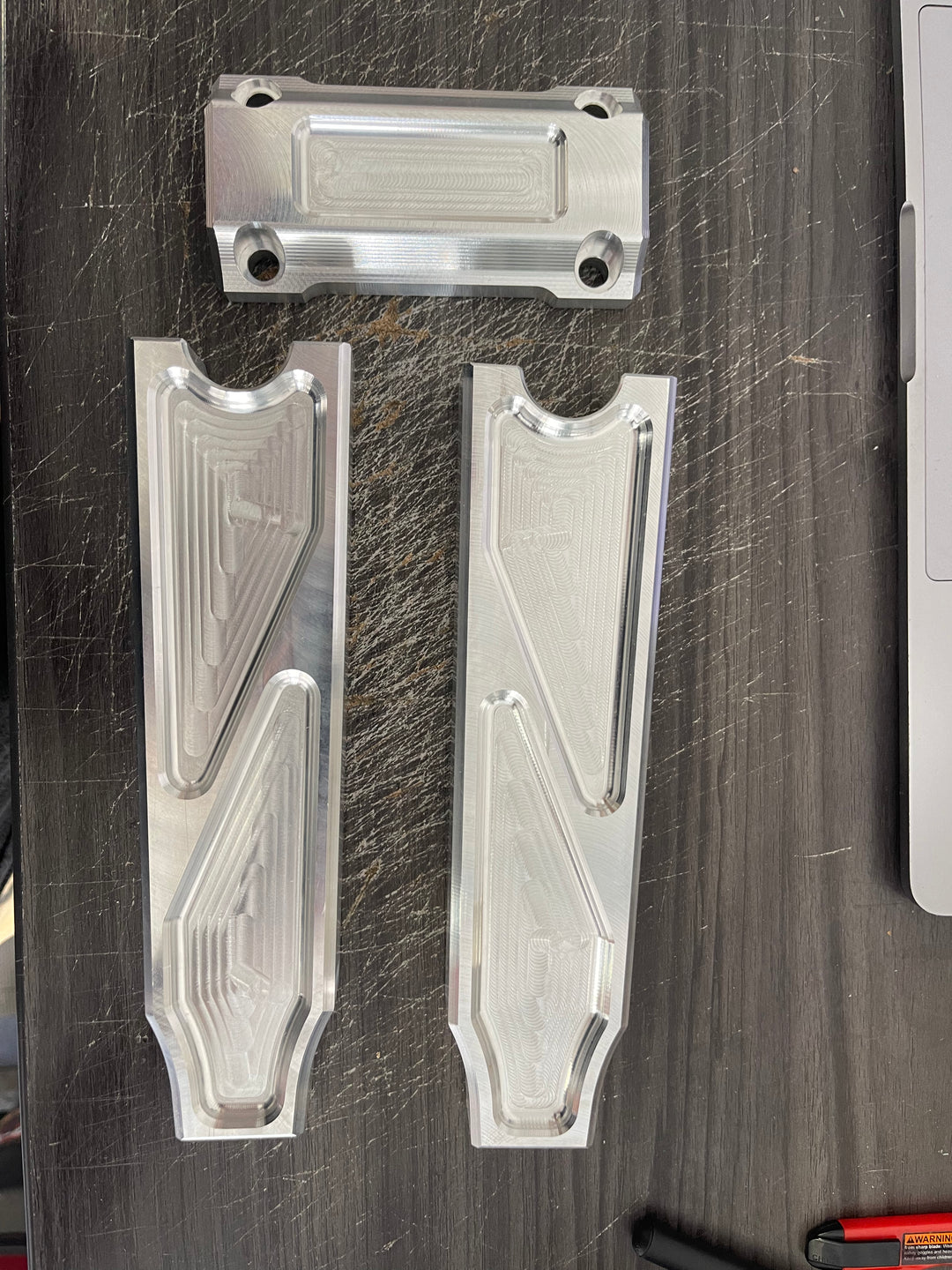 A pair of silver motorcycle bar risers placed on a wooden surface, with engraved details and ratios on the side.