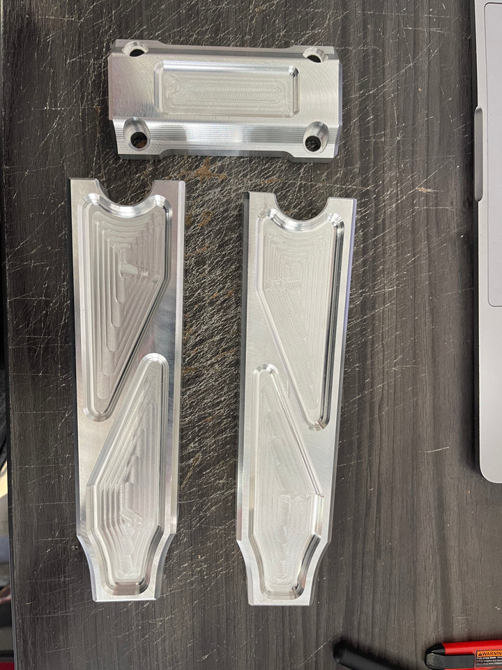 A pair of silver motorcycle bar risers placed on a wooden surface, with engraved details and ratios on the side.