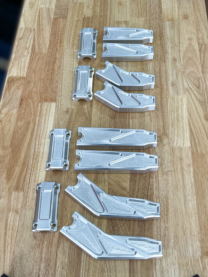 A pair of silver motorcycle bar risers placed on a wooden surface, with engraved details and ratios on the side.