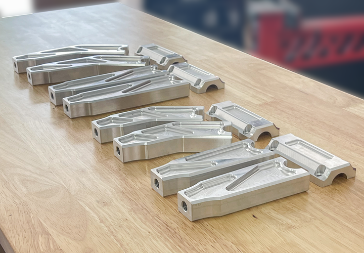 A pair of silver motorcycle bar risers placed on a wooden surface, with engraved details and ratios on the side.