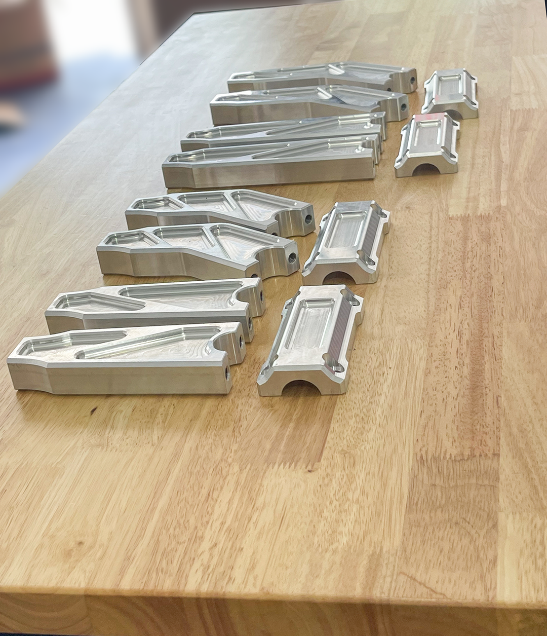 A pair of silver motorcycle bar risers placed on a wooden surface, with engraved details and ratios on the side.