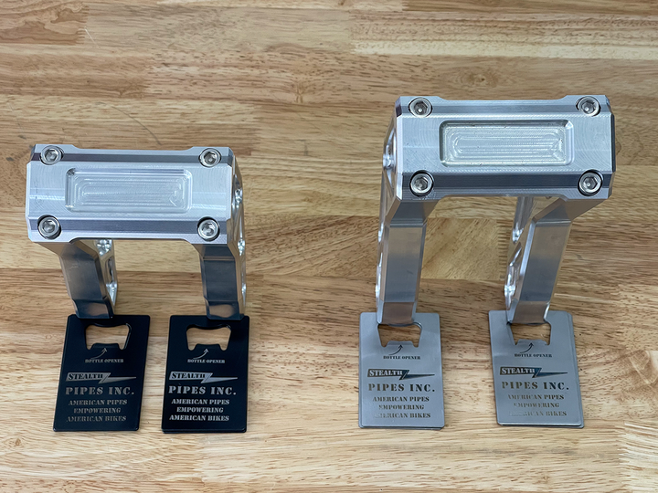 A pair of silver motorcycle bar risers placed on a wooden surface, with engraved details and ratios on the side.