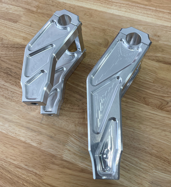 A pair of silver motorcycle bar risers placed on a wooden surface, with engraved details and ratios on the side.