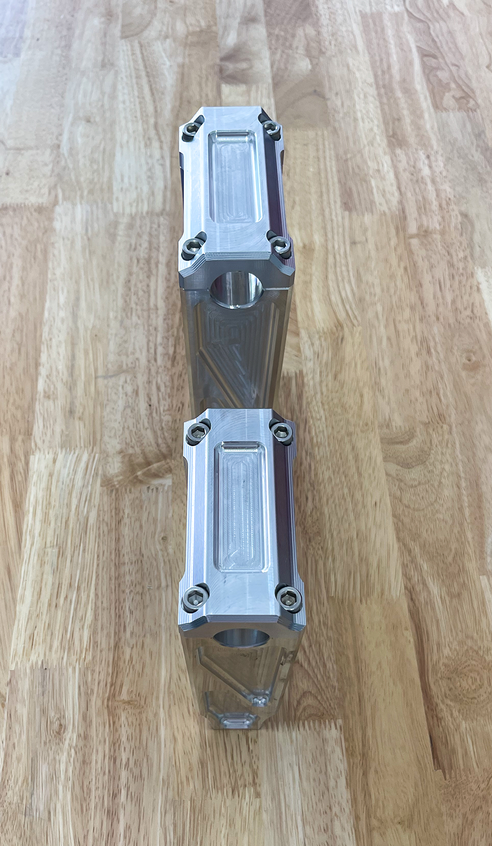 A pair of silver motorcycle bar risers placed on a wooden surface, with engraved details and ratios on the side.
