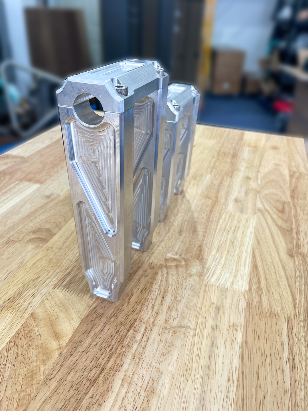 A pair of silver motorcycle bar risers placed on a wooden surface, with engraved details and ratios on the side.