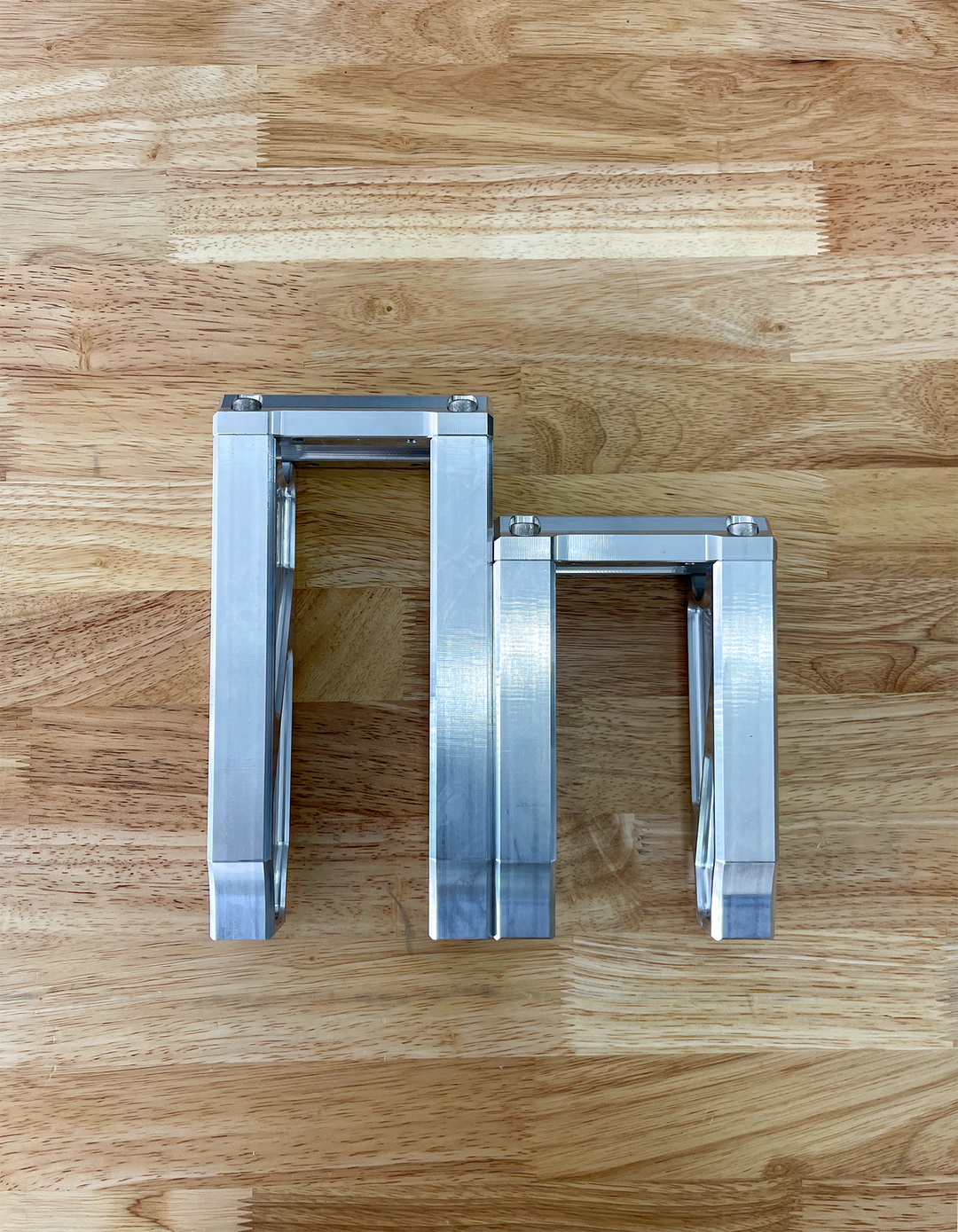 A pair of silver motorcycle bar risers placed on a wooden surface, with engraved details and ratios on the side.