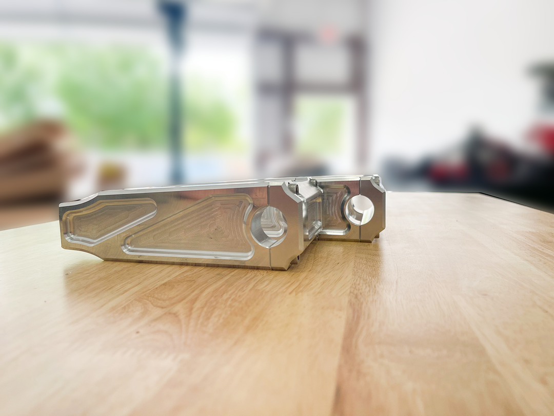A pair of silver motorcycle bar risers placed on a wooden surface, with engraved details and ratios on the side.