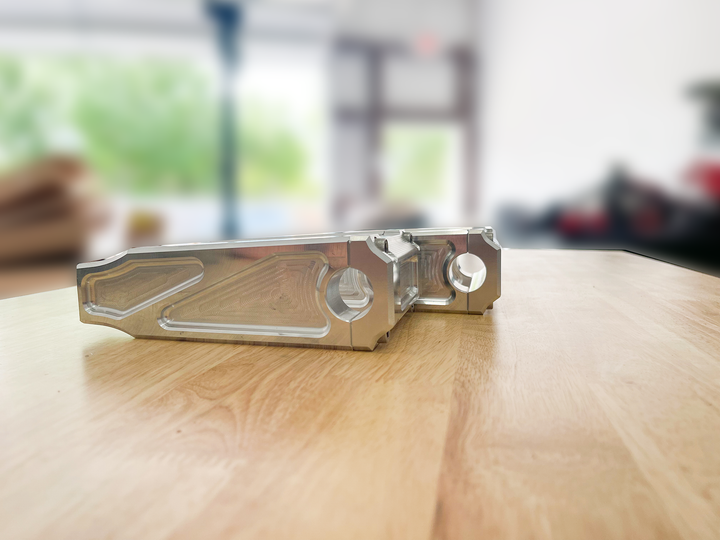 A pair of silver motorcycle bar risers placed on a wooden surface, with engraved details and ratios on the side.