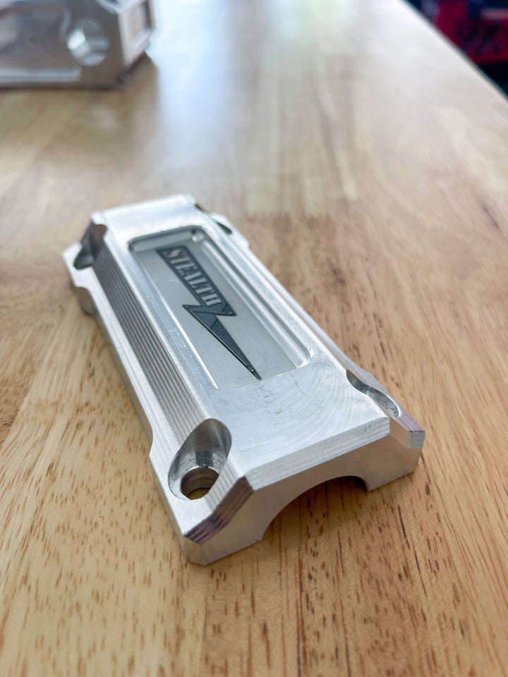 A pair of silver motorcycle bar risers placed on a wooden surface, with engraved details and ratios on the side.