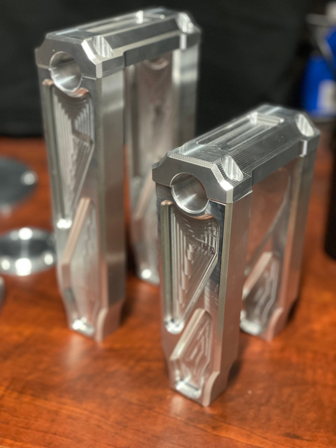 A pair of silver motorcycle bar risers placed on a wooden surface, with engraved details and ratios on the side.